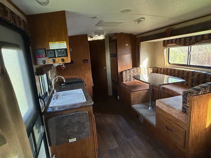 Cozy RV rental interior with a kitchen, dining booth, wooden cabinetry, and bright sunlight streaming in.. Outdoors RV 22BHS 2019