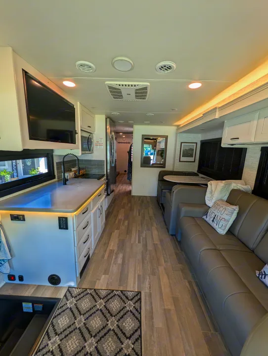 Spacious, modern rv rental interior with a full kitchen, sofa, and dinette. Features wood-look flooring and bright lighting.. Jayco Precept 2025