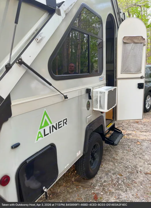 A light-colored A-liner pop-up camper rv rental with an external AC unit, open door, and a person visible inside.. A-Liner Ranger 2025