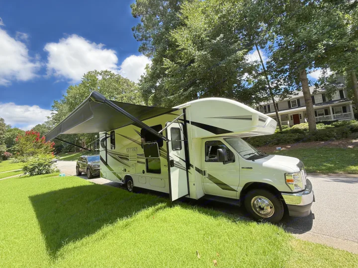 White RV rental (Odyssey Entegra) with awning extended, parked on a lush lawn under sunny skies.. Entegra Coach Odyssey 2023