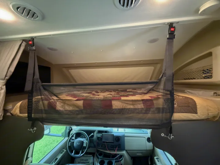 Inside an RV rental: a cozy overhead bunk with safety net, viewed from above the driver's area. Perfect for family travel.. Entegra Coach Odyssey 2023