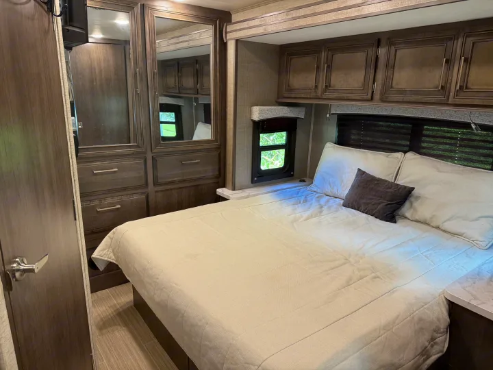 Comfortable RV rental bedroom with a quilted bedspread, mirrored wardrobe, overhead storage, and natural light from the windows.. Entegra Coach Odyssey 2023