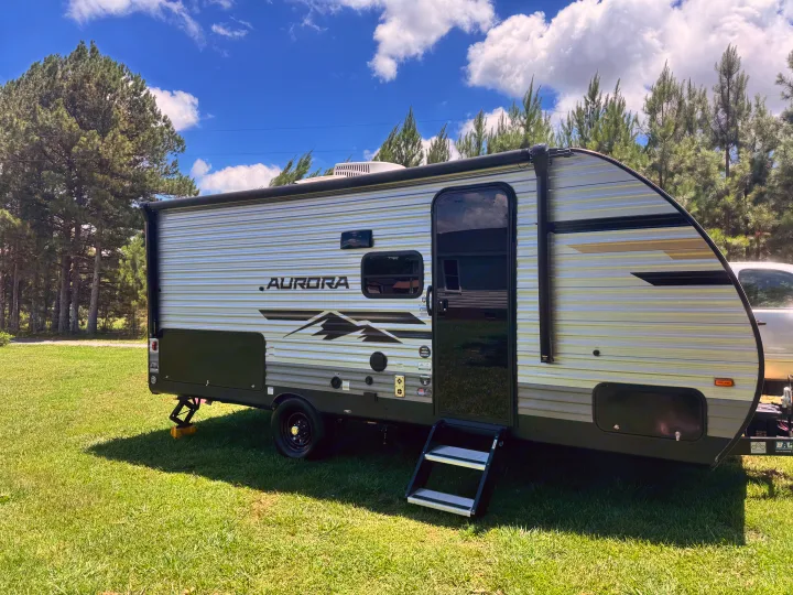 An Aurora travel trailer RV rental sits on green grass under a sunny blue sky, ready for your next outdoor camping adventure.. Forest River Aurora Aurora Light 2026