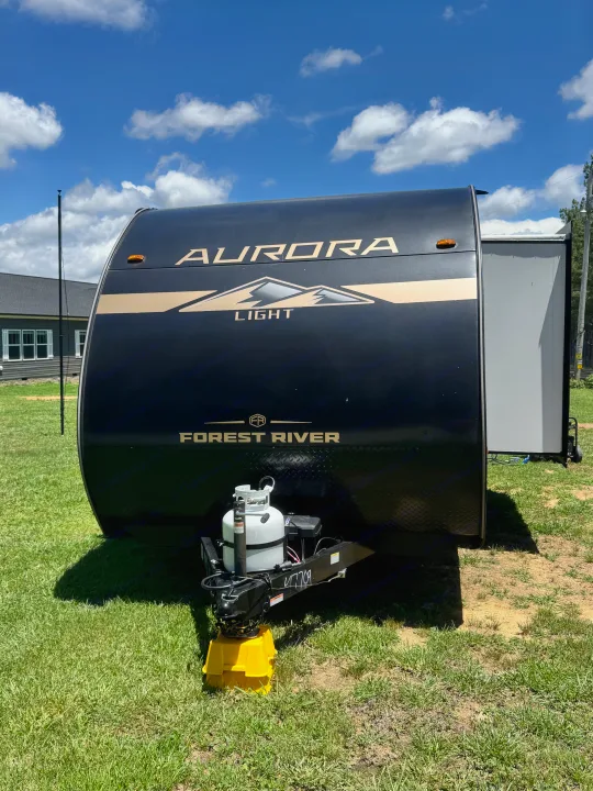Black Forest River Aurora Light travel trailer for rv rental, parked outdoors on a sunny day with blue skies and clouds.. Forest River Aurora Aurora Light 2026
