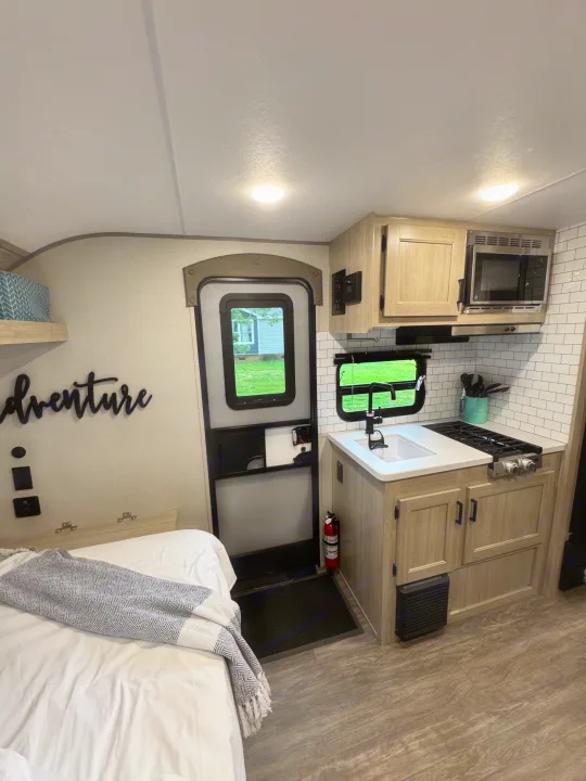 Explore this rv rental's efficient design: a full kitchen with light wood cabinets, subway tile, and cozy bed. Adventure awaits!. Forest River Aurora Aurora Light 2026