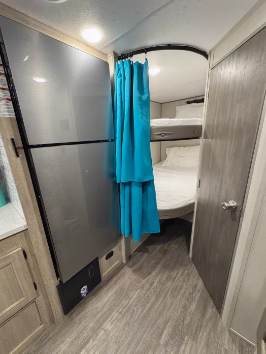 Compact rv rental interior with a fridge, turquoise privacy curtain for bunk beds, and modern wood-look finishes.. Forest River Aurora Aurora Light 2026