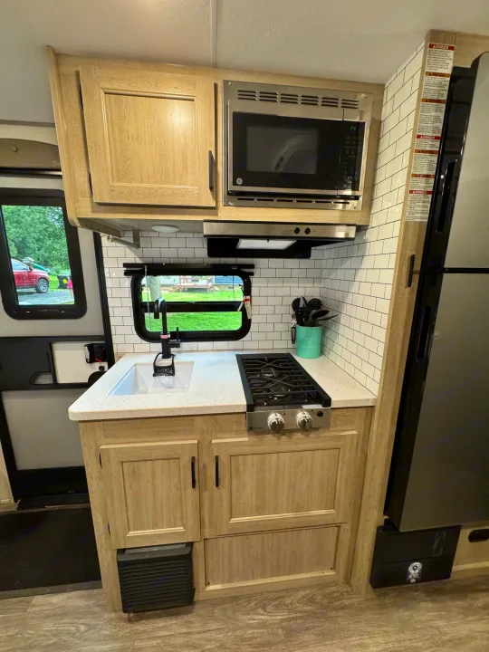 Modern RV rental kitchen featuring a sink, stove, microwave, and refrigerator, complemented by light wood cabinets and subway tiles.. Forest River Aurora Aurora Light 2026