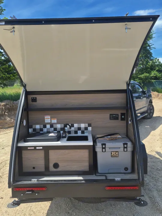RV rental teardrop camper's open outdoor kitchen with sink, cooktop, and K2 cooler for camping adventures.. BUSHWACKER 10HD 2024
