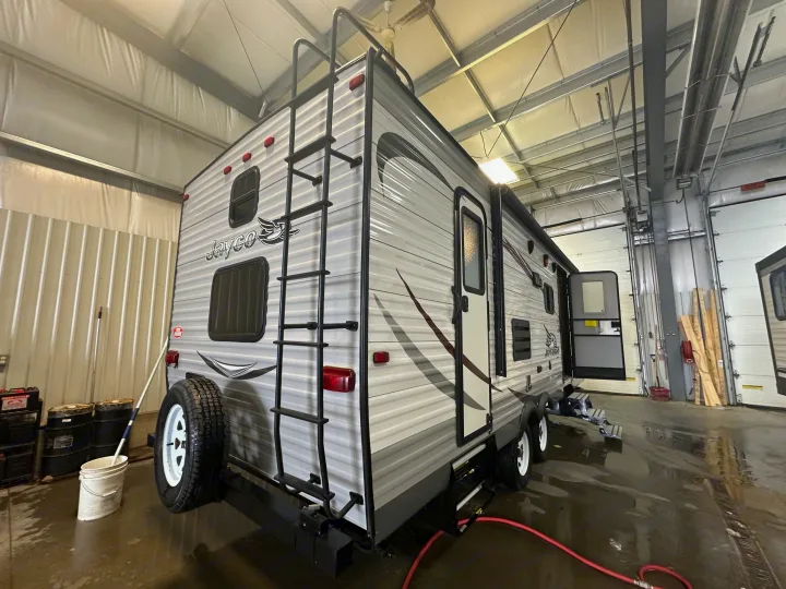 This grey Jayco RV rental, a travel trailer, is seen freshly serviced in a bright bay, door open, rear-view.. Jayco Jay Flight 2015