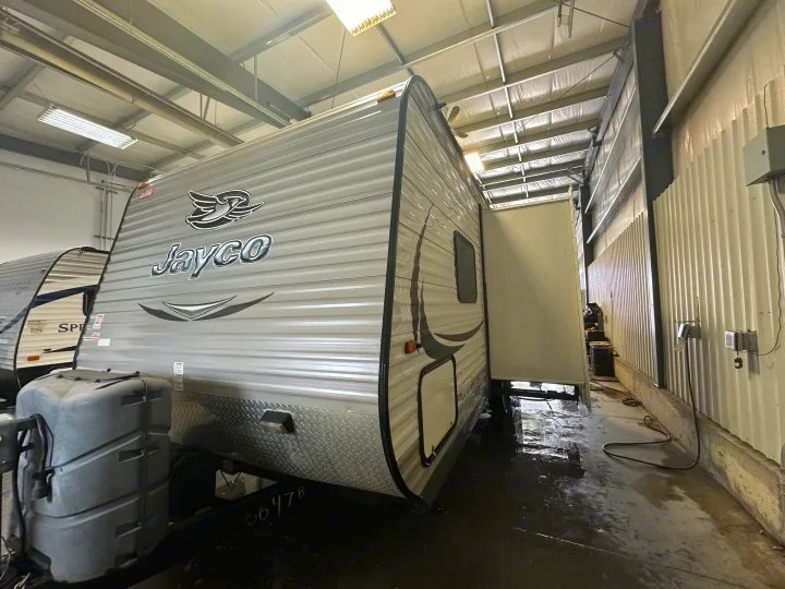 Jayco RV rental travel trailer in a wet indoor service bay with extended slide-out. Ready for maintenance.. Jayco Jay Flight 2015