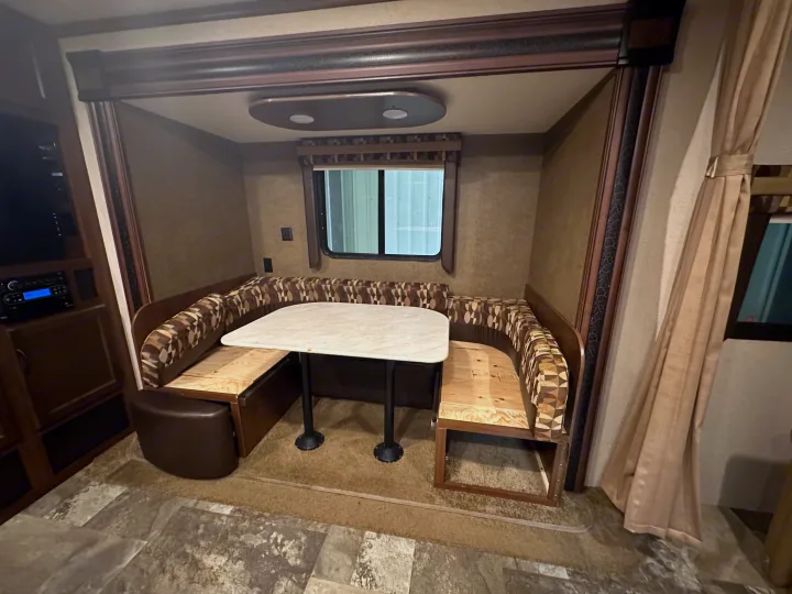 This RV rental features a cozy U-shaped dinette with a light-colored table, patterned cushions, and a window, perfect for dining.. Jayco Jay Flight 2015