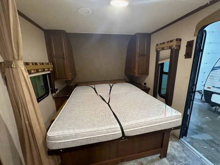 RV rental bedroom featuring a secured bed, wooden cabinets, windows, and an open door showing another RV outside.. Jayco Jay Flight 2015