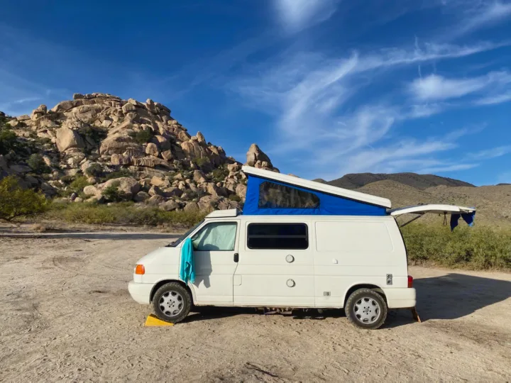 White camper van (RV rental) with blue pop-top in a rugged desert landscape with rocky mountains under blue skies.. Winnebago Eurovan Camper Eurovan Camper 1997