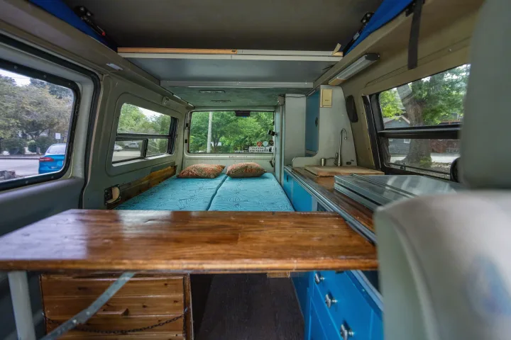 Explore this spacious camper van RV rental interior! Features include a comfy bed, functional kitchen, and wooden table.. Winnebago Eurovan Camper Eurovan Camper 1997
