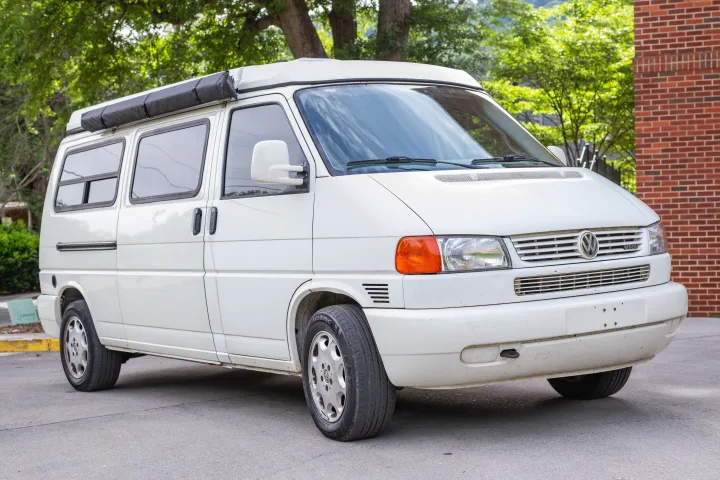 White Volkswagen T4 camper van, featuring a pop-top roof and side awning, ideal for an rv rental adventure.. Winnebago Eurovan Camper Eurovan Camper 1997