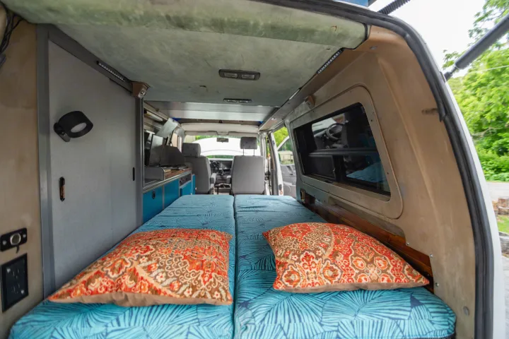 Inside a cozy RV rental camper van: comfortable beds with blue and orange cushions, facing the front seats and kitchen area.. Winnebago Eurovan Camper Eurovan Camper 1997