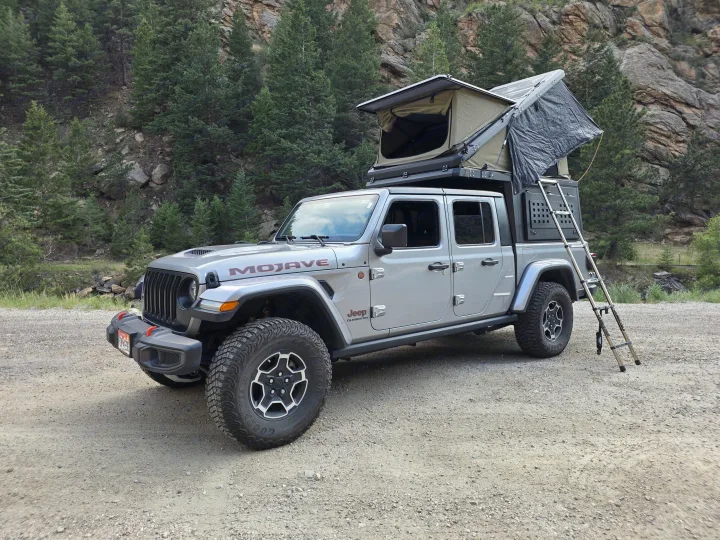 Silver Jeep Gladiator with a deployed rooftop tent, ready for an RV rental off-road camping adventure in the mountains.. jeep Gladiator 2021