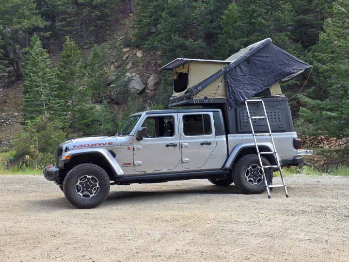 This silver Jeep Gladiator, equipped with a rooftop tent and ladder, makes for an ideal RV rental for off-road overlanding.. jeep Gladiator 2021