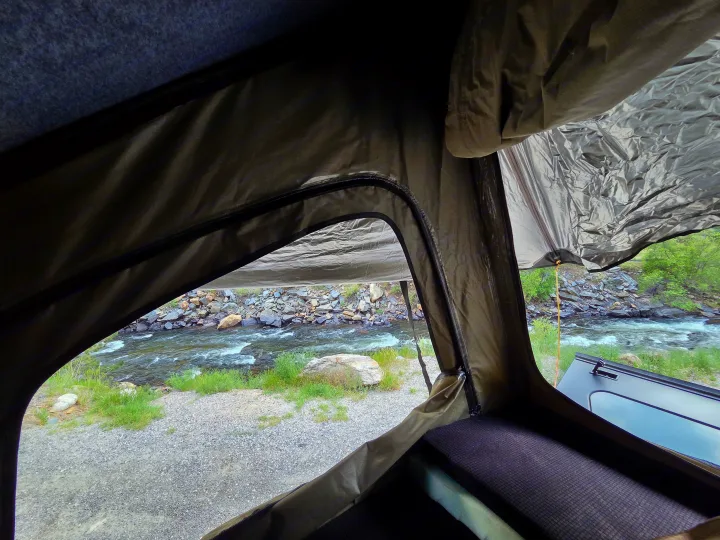 Inside an RV rental rooftop tent, a comfy sleeping area overlooks a scenic river view. Perfect for outdoor adventure.. jeep Gladiator 2021