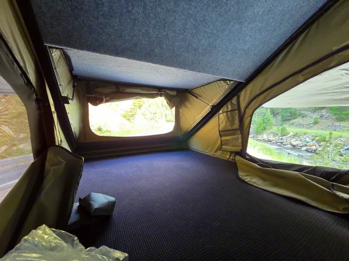 Inside a comfy rv rental rooftop tent, offering scenic river views. Features dark patterned floor, olive walls, and a grey felt ceiling.. jeep Gladiator 2021