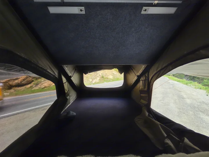Cozy rv rental rooftop tent interior with a dark bed, overhead lights, and a roadside view for your next adventure.. jeep Gladiator 2021