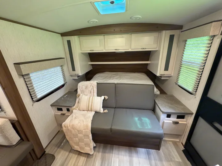 Modern RV rental interior featuring a bed, comfortable sofa with throw, overhead storage, and window blinds.. Cruiser RV MPG 2023