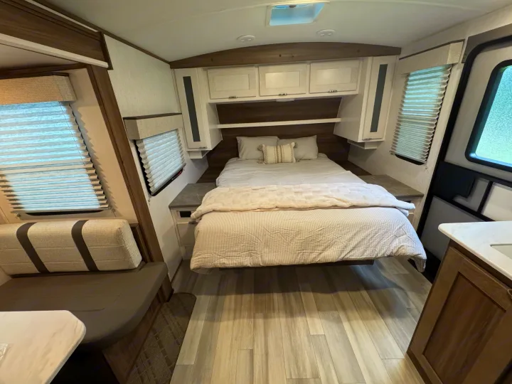 RV rental bedroom with a full bed, overhead cabinets, light wood flooring, and a cozy dinette. Modern, bright interior.. Cruiser RV MPG 2023