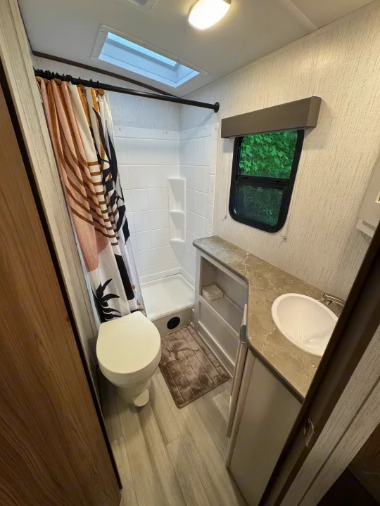 Enjoy the compact, modern bathroom amenities in this rv rental, complete with shower, toilet, sink, and a view through the window.. Cruiser RV MPG 2023
