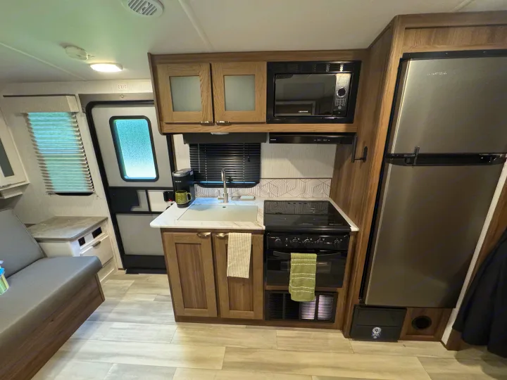Modern RV rental kitchen features a microwave, stove, sink, fridge, and adjacent dinette seating area.. Cruiser RV MPG 2023