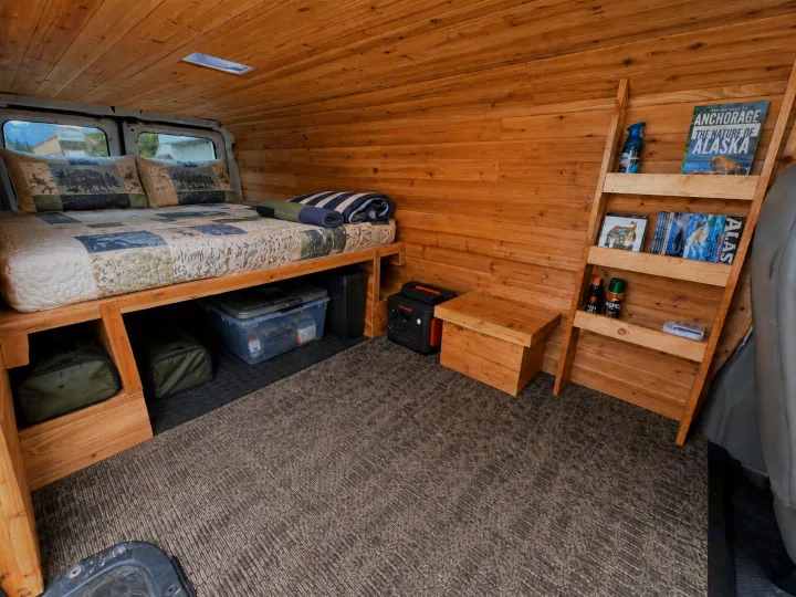 Experience comfort in this RV rental van conversion, showcasing a cozy bed, wooden interior, and smart storage solutions.. Ford Econolline 250s 1998