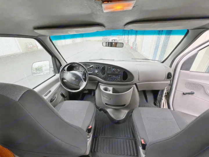 Interior of a van cabin for an rv rental, showing the dashboard, steering wheel, front seats, and a rain-streaked windshield.. Ford Econolline 250s 1998