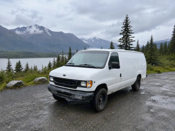 White cargo van (RV rental option) in front of a scenic mountain lake and pine forest on a cloudy, wet day.. Ford Econolline 250s 1998