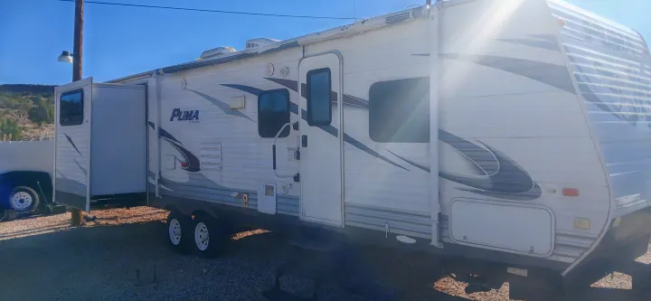 Spacious white Puma RV rental with its slide-out extended, parked on gravel, perfect for your next adventure.. Palomino Puma 2013