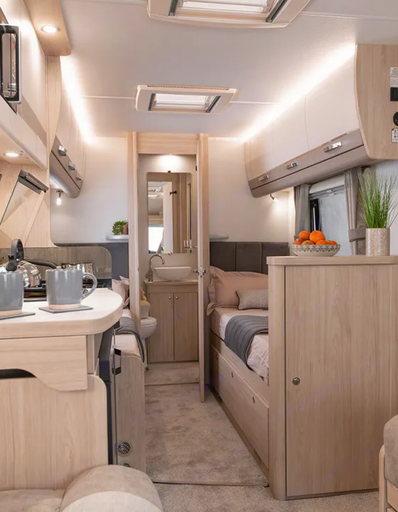 Cozy RV rental interior with light wood accents, showing a compact kitchen on the left, twin beds, and a bathroom through the doorway.. Elddis Whirlwind GT 185 2026
