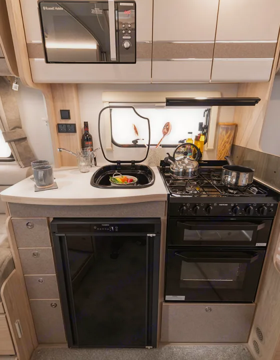 A well-appointed RV rental kitchen features a microwave, sink, gas hob, oven, grill, and fridge for convenient cooking.. Elddis Whirlwind GT 185 2026