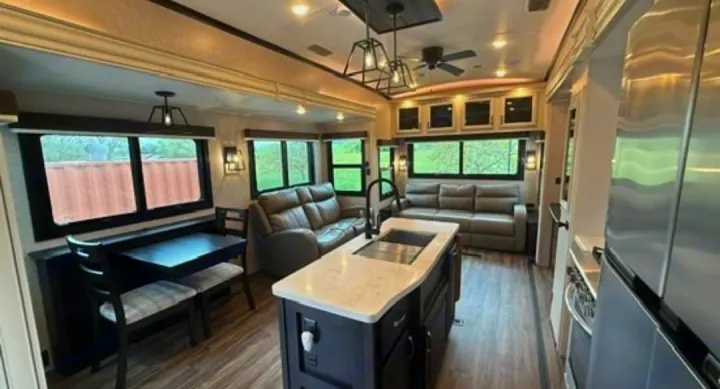 This RV rental's spacious, modern interior features gray sofas, a kitchen island, and a dining area, offering comfortable living space.. Jayco North Point 2023