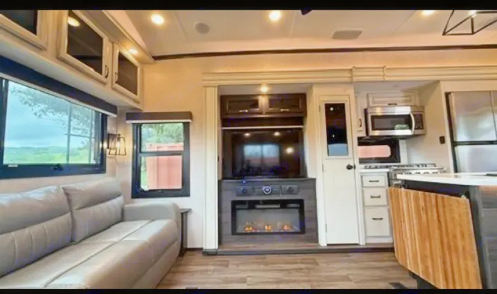 Discover this inviting RV rental interior: a modern living space with sofa, TV, fireplace, and a well-equipped kitchen.. Jayco North Point 2023
