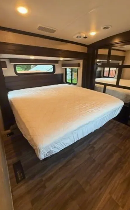 Inside an RV rental: a cozy bedroom features a large bed, dark wood accents, and bunk beds reflected in the mirror.. Jayco North Point 2023