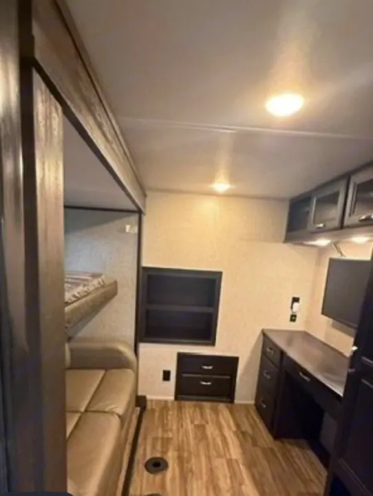 View inside an RV rental: bunk beds, a sofa, built-in desk with TV, and storage cabinets, all in a compact space.. Jayco North Point 2023