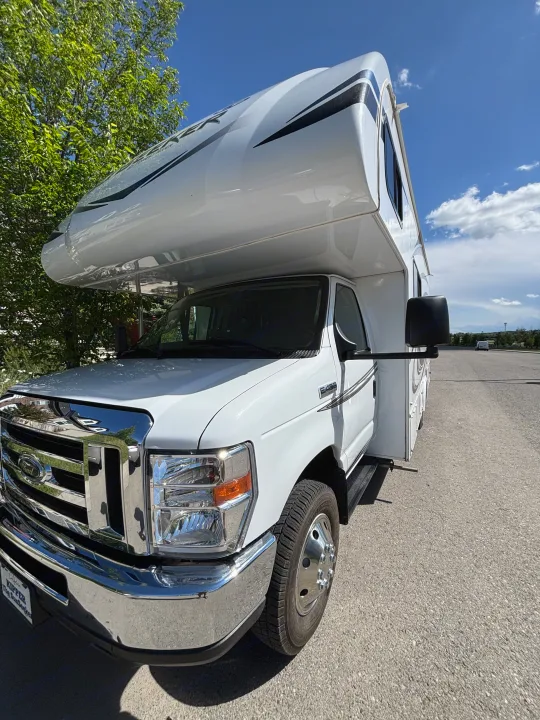Bright white Ford Class C RV rental under a sunny sky. Features a gleaming chrome grille and prominent over-cab sleeping area.. Forest River Sunseeker LE 2020
