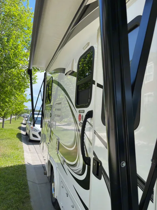 White **rv rental** with an extended awning, parked on a sunny street beside green trees and other vehicles.. Forest River Sunseeker LE 2020