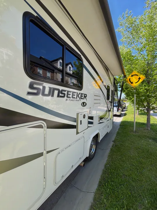 Detailed side view of a white Sunseeker RV, a Forest River motorhome, with its awning extended. Likely an RV rental.. Forest River Sunseeker LE 2020
