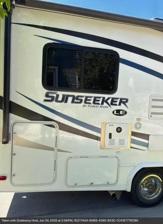 Side view of a white Forest River Sunseeker LE RV rental, featuring black stripes, an extended awning, and various exterior compartments.. Forest River Sunseeker LE 2020