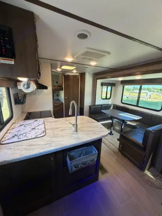 Inside this **rv rental**: a bright kitchen with island, comfy dining booth, and rear bunk beds, ideal for travel.. Keystone RV Passport Ultra Lite 2019