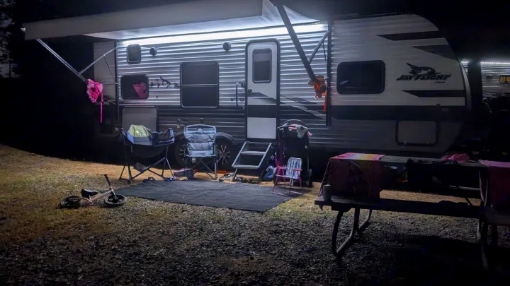 Illuminated RV rental at a nighttime campsite, showing chairs, a child's bike, and a picnic table for outdoor relaxation.. Jayco Jay Flight SLX 2023