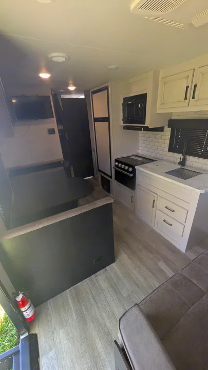 Bright rv rental interior: kitchen with stove, sink, microwave; dining booth, sofa, & TV. Compact, modern living space.. Jayco Jay Flight SLX 2023