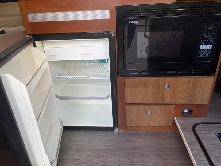 This rv rental kitchen features an open refrigerator, a High Pointe microwave with digital controls, and wood-paneled storage drawers.. Winnebago Travato 2016