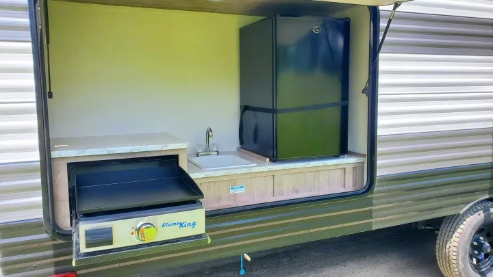 This RV rental's open outdoor kitchen includes a pull-out griddle, sink, and secured mini-fridge, ready for camping meals.. Gulf Stream Ameri-Lite 2024