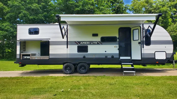White and grey Ameri-Lite RV rental, featuring an extended awning and an open outdoor kitchen setup.. Gulf Stream Ameri-Lite 2024