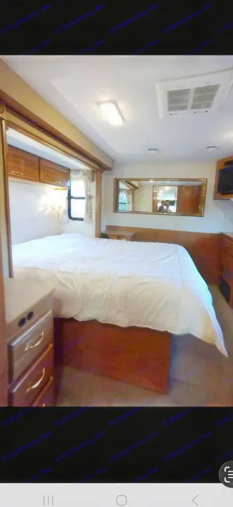 RV rental bedroom featuring a clean bed, wooden cabinetry, and a wall mirror. Explore comfortably on your next journey.. Ford 1F6NF3S740A06630 2004
